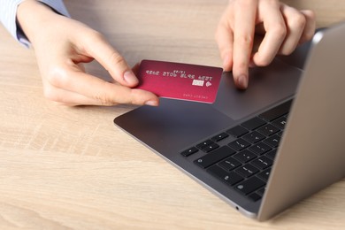 Photo of Online payment. Woman with credit card typing on laptop at wooden table, closeup