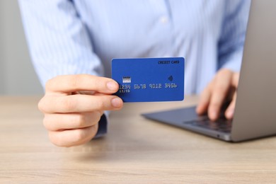 Photo of Online payment. Woman with credit card typing on laptop at wooden table, closeup