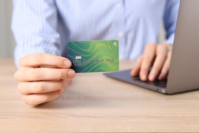 Photo of Online payment. Woman with credit card typing on laptop at wooden table, closeup
