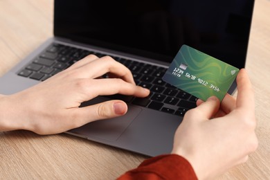 Photo of Online payment. Woman with credit card typing on laptop at wooden table, closeup