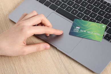 Photo of Online payment. Woman with credit card typing on laptop at wooden table, closeup