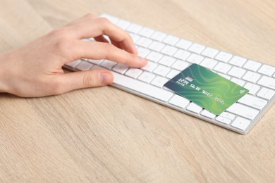 Photo of Online payment. Woman with credit card typing on computer keyboard at wooden table, closeup