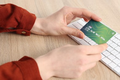 Photo of Online payment. Woman with credit card and computer keyboard at wooden table, closeup