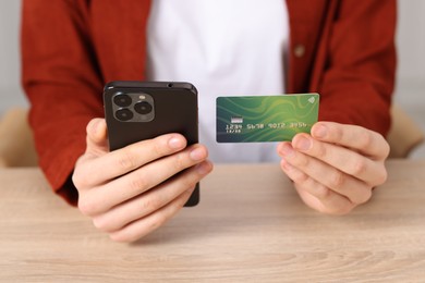 Photo of Woman with credit card and smartphone paying online at wooden table, closeup