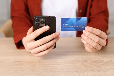 Photo of Woman with credit card and smartphone paying online at wooden table, closeup