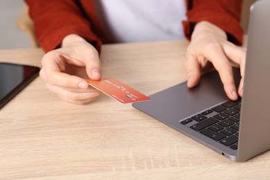Photo of Online payment. Woman with credit card typing on laptop at wooden table, closeup