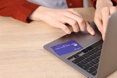 Photo of Online payment. Woman with credit card typing on laptop at wooden table, closeup