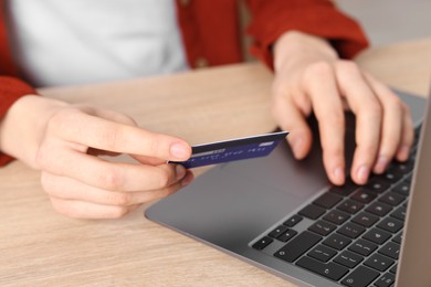 Photo of Online payment. Woman with credit card and laptop at wooden table, closeup