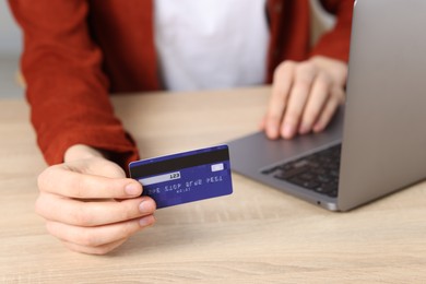 Photo of Online payment. Woman with credit card and laptop at wooden table, closeup