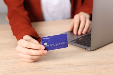 Photo of Online payment. Woman with credit card and laptop at wooden table, closeup