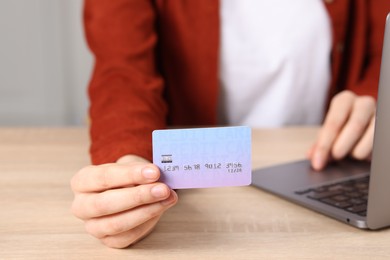 Photo of Online payment. Woman with credit card and laptop at wooden table, closeup