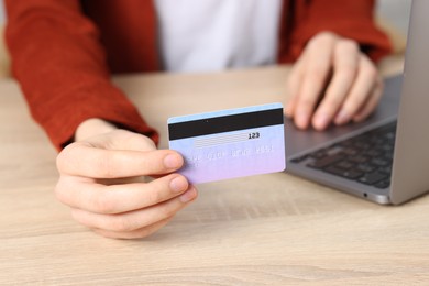 Photo of Online payment. Woman with credit card and laptop at wooden table, closeup