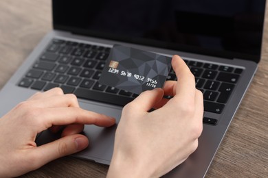 Photo of Online payment. Woman with credit card using laptop at wooden table, closeup