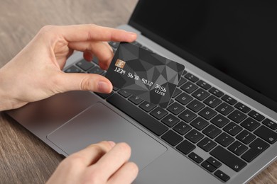 Photo of Online payment. Woman with credit card using laptop at wooden table, closeup