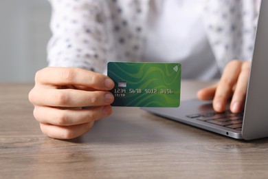 Photo of Online payment. Woman with credit card and laptop at wooden table, closeup