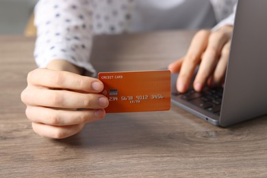 Photo of Online payment. Woman with credit card and laptop at wooden table, closeup