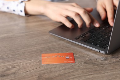 Photo of Online payment. Woman typing on laptop at wooden table, focus on credit card