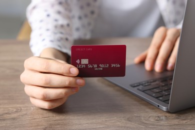 Photo of Online payment. Woman with credit card and laptop at wooden table, closeup