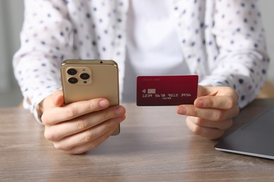 Photo of Woman with credit card and smartphone paying online at wooden table, closeup