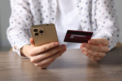 Photo of Woman with credit card and smartphone paying online at wooden table, closeup
