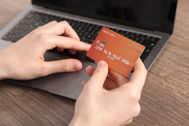 Photo of Online payment. Woman with credit card typing on laptop at wooden table, closeup