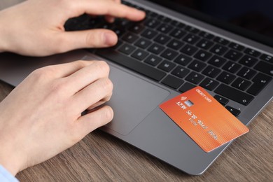 Photo of Online payment. Woman with credit card typing on laptop at wooden table, closeup