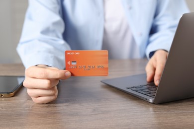 Photo of Online payment. Woman with credit card and laptop at wooden table, closeup