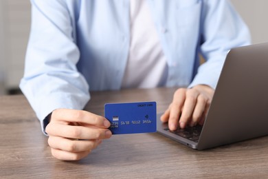 Photo of Online payment. Woman with credit card and laptop at wooden table, closeup