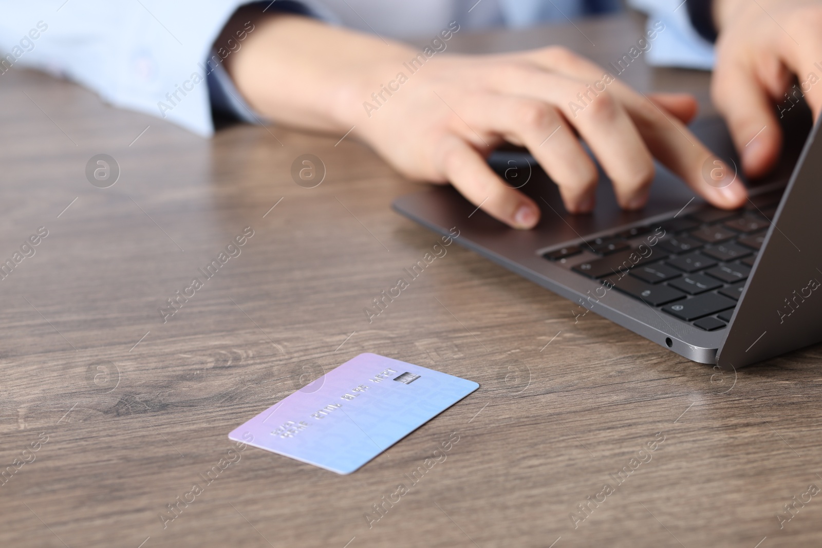 Photo of Online payment. Woman typing on laptop at wooden table, focus on credit card