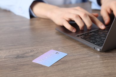 Photo of Online payment. Woman typing on laptop at wooden table, focus on credit card
