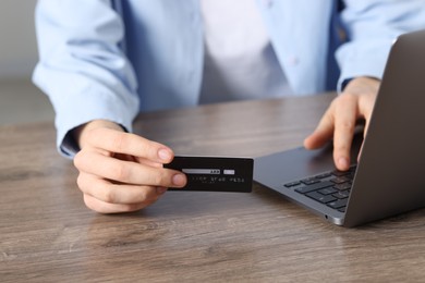 Photo of Online payment. Woman with credit card and laptop at wooden table, closeup