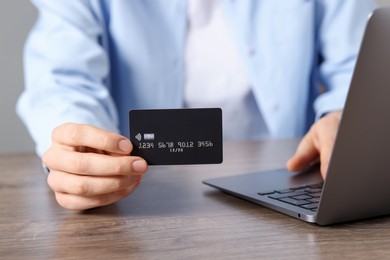 Photo of Online payment. Woman with credit card and laptop at wooden table, closeup