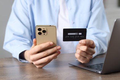 Photo of Woman with credit card, smartphone and laptop paying online at wooden table, closeup