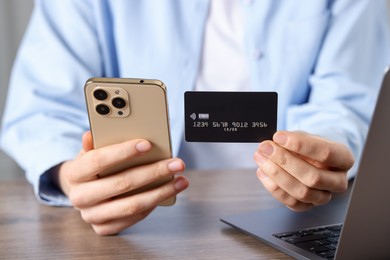 Photo of Woman with credit card, smartphone and laptop paying online at wooden table, closeup