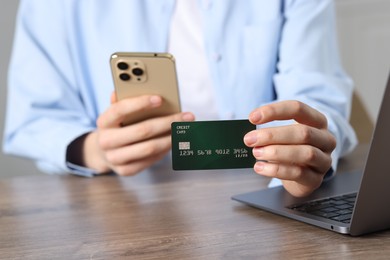 Photo of Woman with credit card, smartphone and laptop paying online at wooden table, selective focus