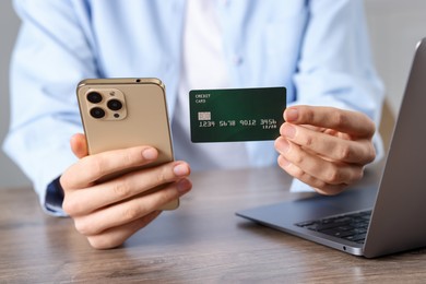 Photo of Woman with credit card, smartphone and laptop paying online at wooden table, closeup