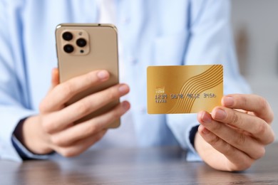 Photo of Woman with credit card and smartphone paying online at table, selective focus