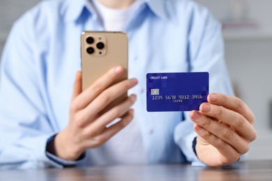 Photo of Woman with credit card and smartphone paying online at table, selective focus