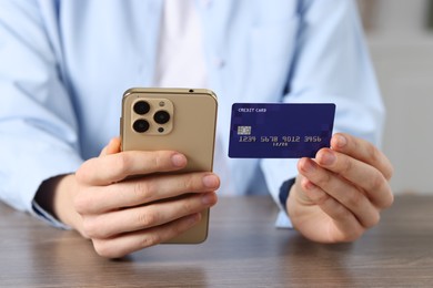 Photo of Woman with credit card and smartphone paying online at wooden table, closeup