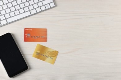 Photo of Online payment. Credit cards, smartphone and computer keyboard on light wooden table, flat lay. Space for text