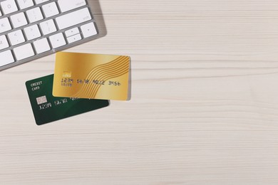 Photo of Online payment. Credit cards and computer keyboard on light wooden table, flat lay. Space for text