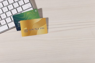 Photo of Online payment. Credit cards and computer keyboard on light wooden table, top view. Space for text