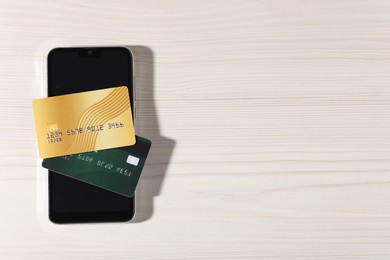 Photo of Online payment. Credit cards and smartphone on light wooden table, top view. Space for text
