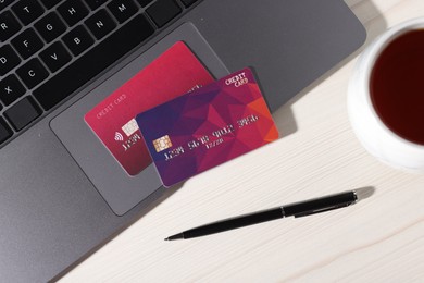 Photo of Online payment. Credit cards, pen and laptop on light wooden table, flat lay