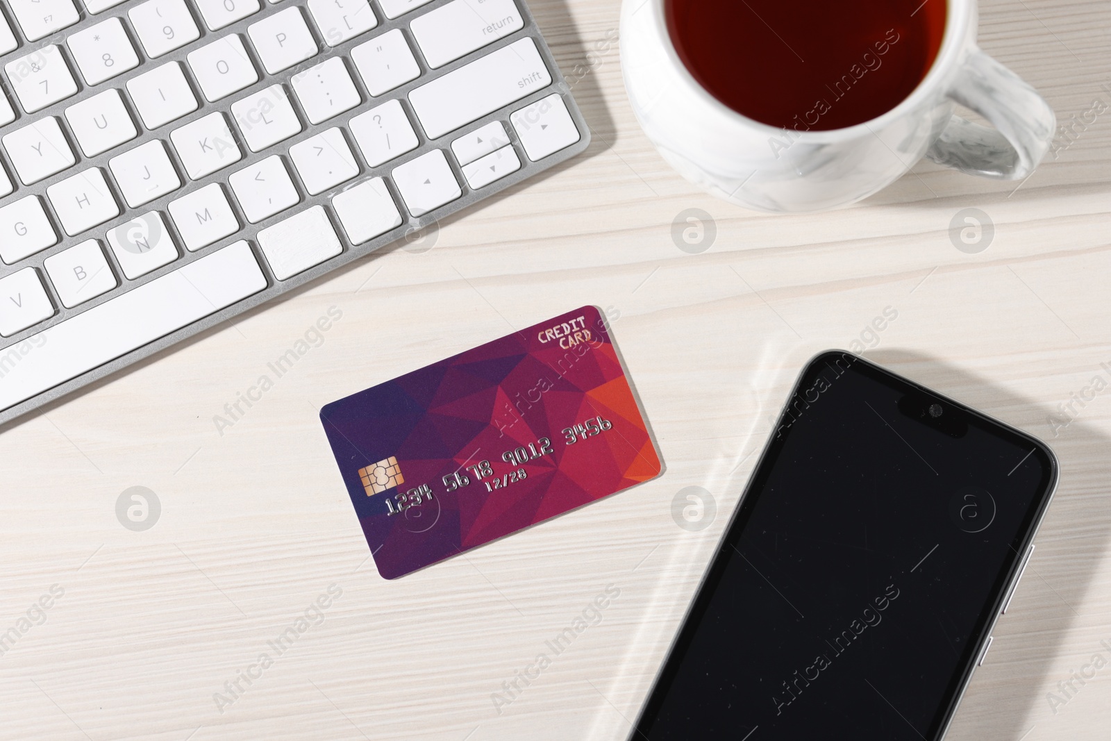 Photo of Online payment. Credit card, smartphone, cup of tea and computer keyboard on light wooden table, flat lay