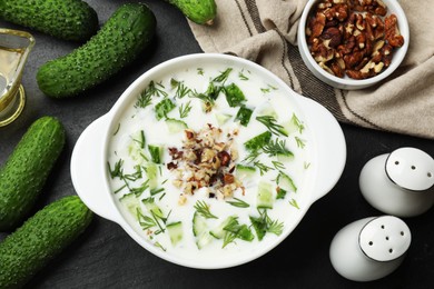 Photo of Fresh tasty cucumber soup and ingredients on black table, flat lay