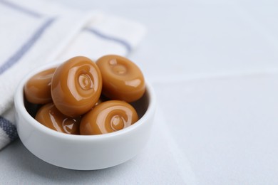 Photo of Tasty sweet caramel candies on white tiled table, closeup. Space for text