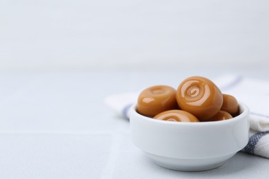 Photo of Tasty sweet caramel candies on white tiled table, closeup. Space for text