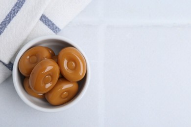 Photo of Tasty sweet caramel candies on white tiled table, top view. Space for text