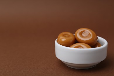 Photo of Tasty sweet caramel candies on brown background, closeup. Space for text